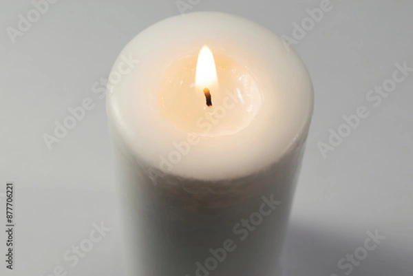 Fototapeta A lighted white candle burning isolated on white background with low light shadow