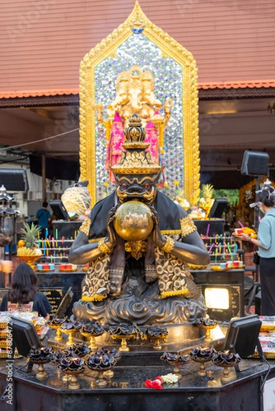 Fototapeta Statue of Rahu swallowing the moon, black and gold color, with Ganesha in the back, which is worshipped by many Buddhists and often visited to pay homage at Bang Yai Temple, Nonthaburi, Thailand.