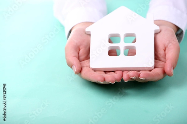 Fototapeta Female hands holding house on color background