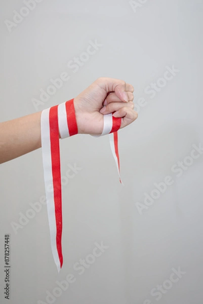 Fototapeta A woman's hand holds a red and white ribbon as a symbol of the Indonesian flag. Isolated on white background