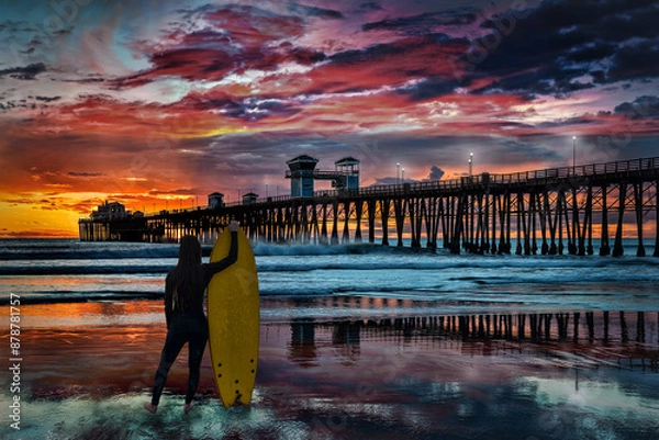 Obraz A female silhouetted surfer takes a minute to admire the colorful sunset at the Oceanside Pier, Oceanside, California, USA.