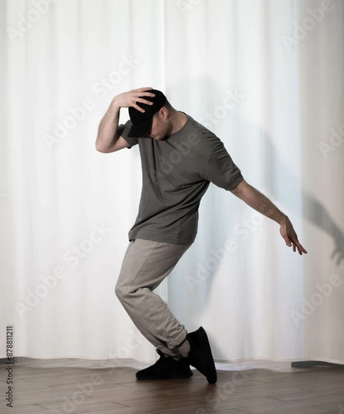 Fototapeta Dance in motion, pose of a man in hip-hop style clothes. Sports dancing guy in training poses. Dance training at home.