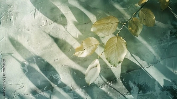 Fototapeta Sunlight filters through leaves, casting shadows on a textured surface, creating a serene autumn scene with yellow leaves
