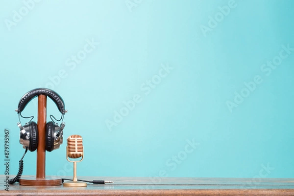 Obraz Golden microphone and retro headphones standing on wooden table front mint blue background. Vintage style filtered photo