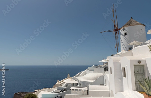 Fototapeta View of traditional white Greek architecture with a windmill on a sunny day against a clear blue sky.
