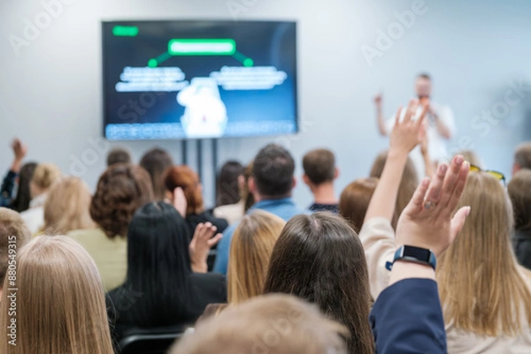 Obraz Engaged audience raising hands in a business presentation, indicating active participation and an interactive Q&A session. Ideal for concepts of learning, teamwork, and seminars.