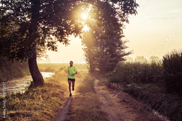 Fototapeta Ragazzo che corre all'alba su strada di campagna in estate
