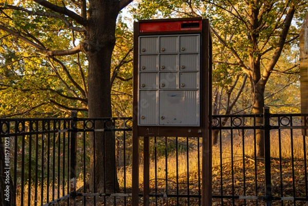 Fototapeta Autumnal scene with mailbox units - golden hour lighting casts warm tones on foliage - wrought iron fence frames composition - tranquil suburban atmosphere. Taken in Toronto, Canada.