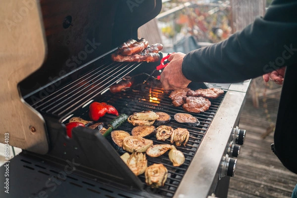 Obraz Person Grilling Meat and Vegetables on a Big Home Gas Grill with Hot Flames During Summer Season on a Sunny Day