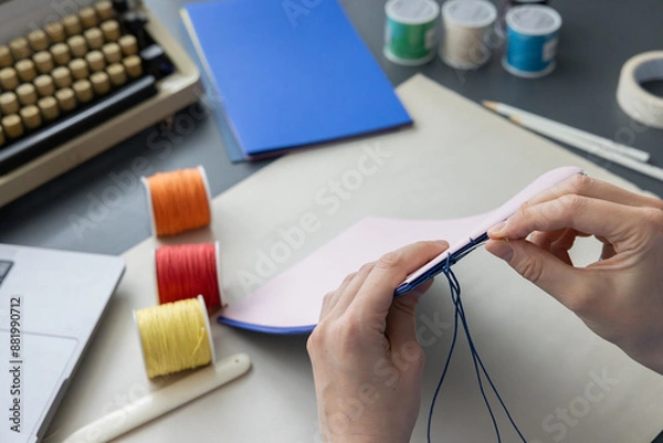 Fototapeta High-quality image of a person binding a book using traditional coptic stitch technique. DIY bookbinding, handcrafting, artisan book, handmade, coptic stitch, binding tools, creative, detailed process