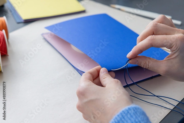 Fototapeta High-quality image of a person binding a book using traditional coptic stitch technique. DIY bookbinding, handcrafting, artisan book, handmade, coptic stitch, binding tools, creative, detailed process