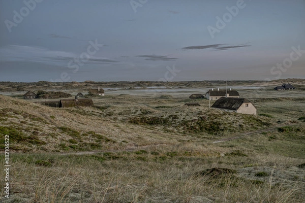 Fototapeta thatched houses scattered in the dunes when the fog settles in the evening