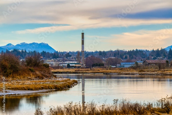 Fototapeta 2022-12-04 THE STILLAGUAMISH RIVER WINDING THROUGH STANWOOD WASHINGTON WITH A SMOKE STACK AND BUILDINGS IN THE BACKGROUND NEAR CAMANO ISLAND WASHINGTON