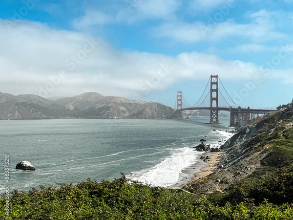 Fototapeta Coastal view of the Golden Gate bridge in San Francisco. American iconic landmark. Cliffs and grass frame the picture. Waves in the bay water. Light fog.