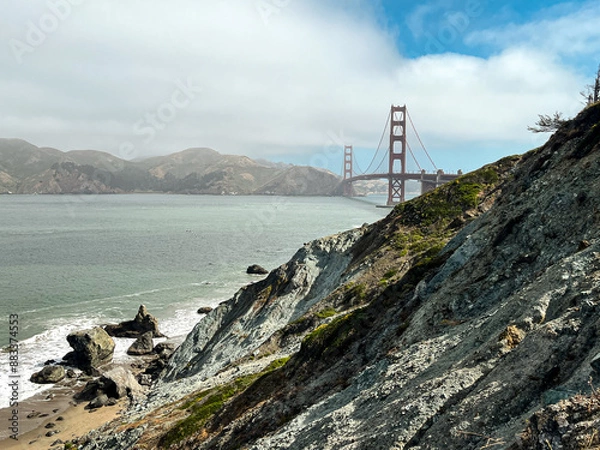 Fototapeta Coastal view of the Golden Gate bridge in San Francisco. American iconic landmark. Cliffs and grass frame the picture. Waves in the bay water. Light fog.