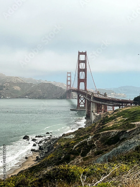 Fototapeta Coastal view of the Golden Gate bridge in San Francisco. American iconic landmark. Cliffs and grass frame the picture. Waves in the bay water. Light fog.