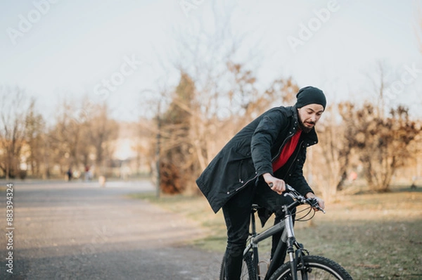 Fototapeta Young man in casual attire enjoys a bike ride in an urban park at sunset, exuding a sense of freedom and relaxation.
