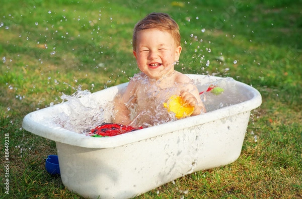 Fototapeta A small happy baby bathed in the bath and playing in a bath with