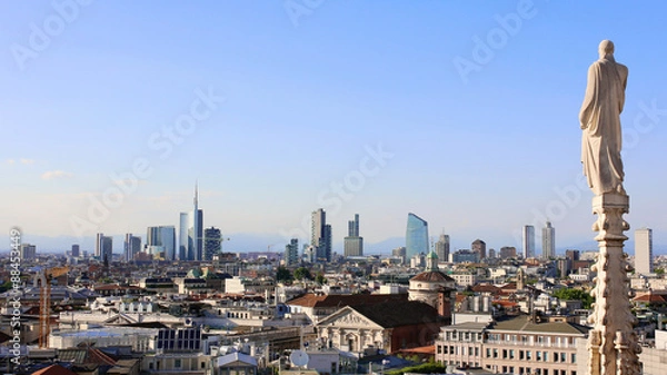 Fototapeta Panoramic view of Milan skyline from Duomo cathedral. Religious statue faces to the buildings of the financial district. The Alps mountains on the background.