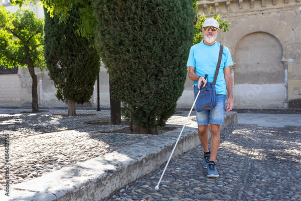 Fototapeta A mature blind man uses a white cane to guide himself through a historic park. This image highlights his independence and determination. and captures a moment of resilience and empowerment. Front view