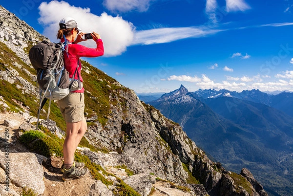 Fototapeta Adventurous athletic female hiker taking a photo with her cellphone of jagged mountains in the in the Pacific Northwest.
