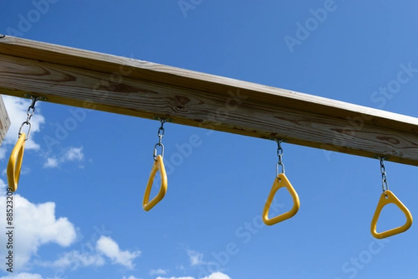 Fototapeta Monkey bar rings hanging from wooden playset with blue sky in background