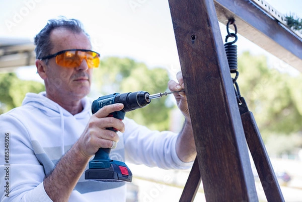 Obraz Man in protective eyewear using power drill outdoors