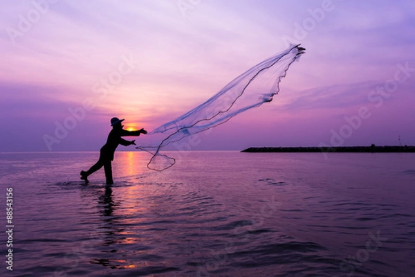 Fototapeta Fisherman throwing net at sunset.