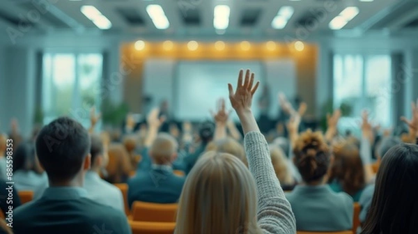 Fototapeta Audience members raising hands during a seminar or conference, implying active participation and engagement in a modern, well-lit venue.