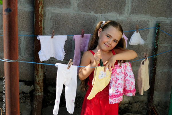 Obraz little girl washes children's clothes and hangs them to dry on a line