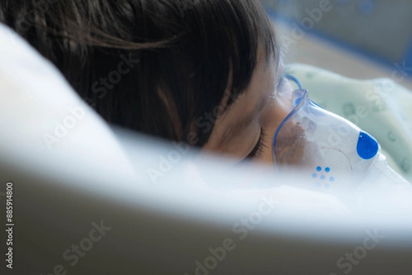 Fototapeta an Asian toddler boy has Cold or Flu or influenza or asthma or pneumonia disease and need nebulizations,Sick boy rest on patient bed in hospital and has inhalation therapy by the mask of inhaler.Sick 