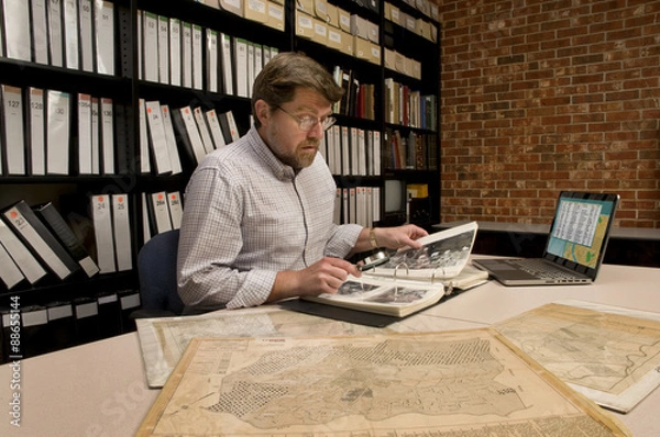 Fototapeta Researcher in Archive Examining Maps and Other Archival Material