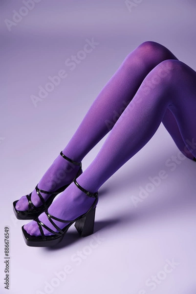 Obraz A young woman stands confidently in high heels and vibrant purple stockings against a purple background in a studio setting.