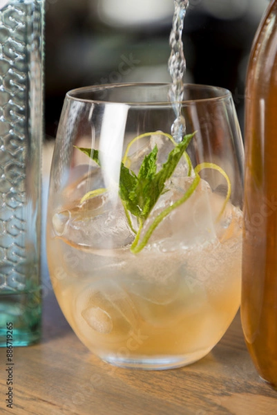 Fototapeta Gin being poured into a gin cocktail in a low ball tumbler with ice and a mint leaf.