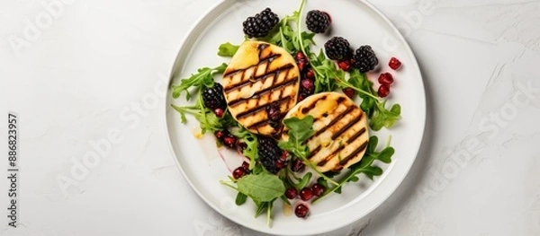 Fototapeta A delicious and nutritious meal idea featuring grilled Halloumi cheese, blackberries, pomegranate seeds, and fresh rocket on a white wooden backdrop. Top-down view with space for text or images.