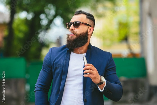 Fototapeta man with a beard smokes electronic cigarette