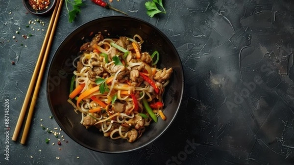 Fototapeta Close-up of delicious stir-fry noodles with meat and vegetables in wok on grey textured table, top view. Perfect for Asian food lovers.