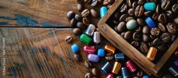 Fototapeta Wooden box holds coffee beans and colorful capsules on a table offering a copy space image from above