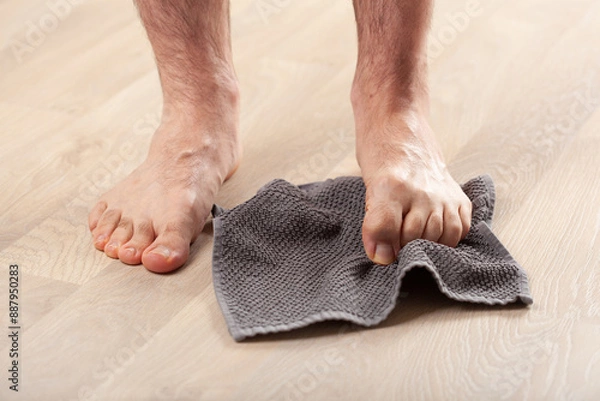 Fototapeta man doing flatfoot correction gymnastic exercise grabbing towel at home