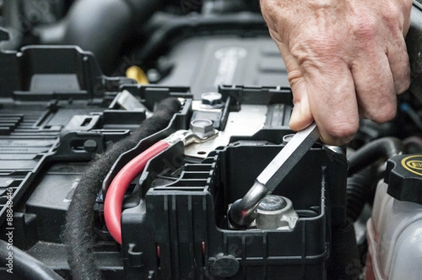 Fototapeta Mani che serrano il morsetto della batteria nel motore di un'automobile con una chiave