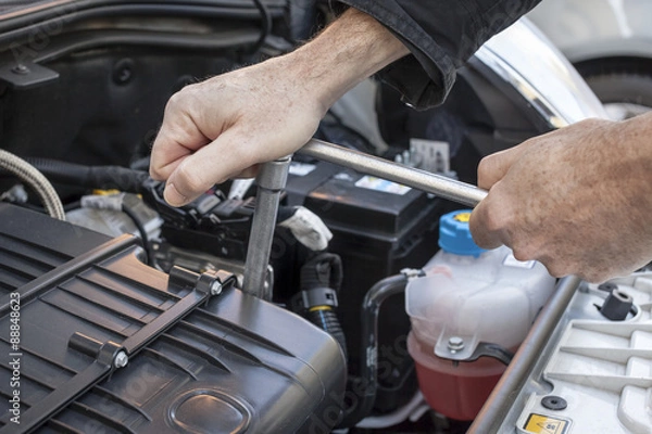 Fototapeta Mani che riparano un motore di automobile con una chiave