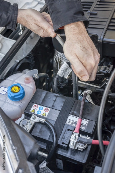 Fototapeta Mani che serrano la batteria nel motore di un'automobile con una chiave