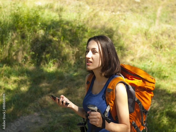 Fototapeta A young girl with a backpack use the phone.