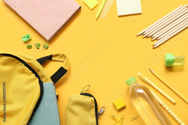 Fototapeta Frame made of school backpack with different stationery supplies on yellow background
