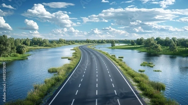 Fototapeta A scenic highway cutting through a lush landscape with rivers and greenery under a blue sky with fluffy clouds on a sunny day.