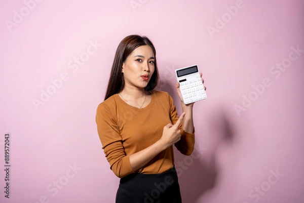 Fototapeta A woman is holding a calculator and pointing at it