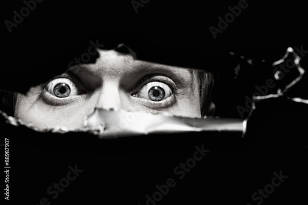 Fototapeta Scary eyes of a man spying through a hole in the wall