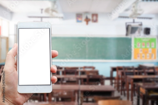 Fototapeta Learning conceptual- Focused on left hand holding mobile with Classroom blurred background
