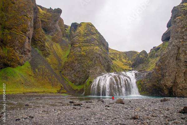 Fototapeta person sitting in front of a tranquil waterfall on a cloudy day in Iceland