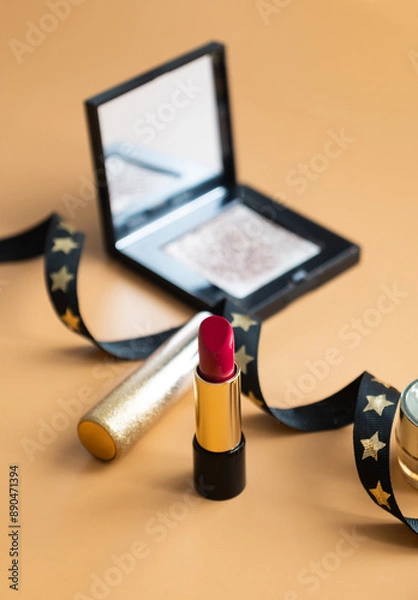 Fototapeta A shot of red lipstick with make up palette and black ribbon with dark orange color isolated background 